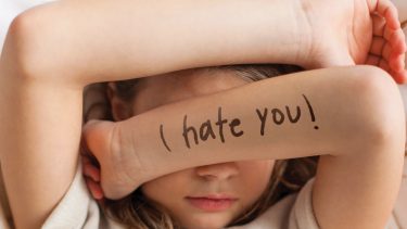 Kid folding their arms over their face. On one arm "I hate you!" is written in marker