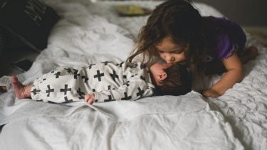 Toddler kissing baby on the forehead in bed