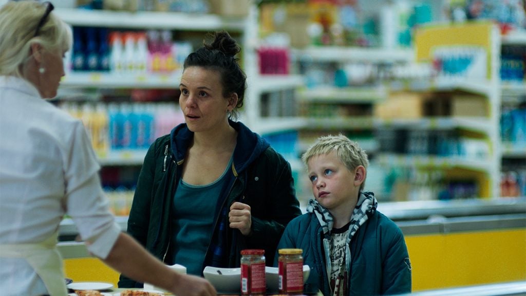 Promo image for And Breathe Normally showing a mom and son at the grocery store check out line
