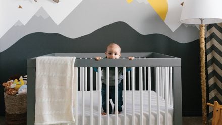 baby in a grey and white crib with mountain wall decals in the nursery