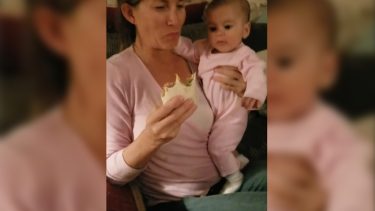 Mom holding baby and eating a burrito while the baby is staring at the burrito