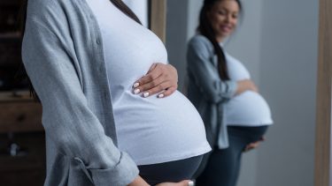 Pregnant woman looking in mirror holding belly