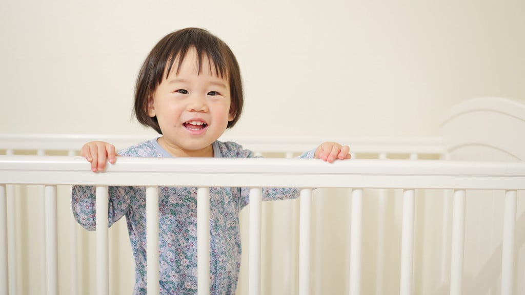 12-month-old baby in floral pyjamas standing up in a white crib