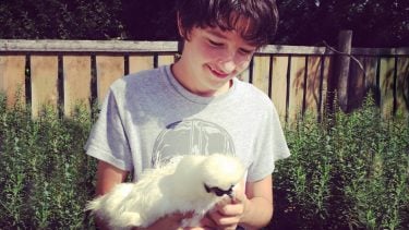 Boy holding his pet chicken and smiling