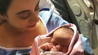 Women in hospital gown holds her newborn baby in a pink blanket