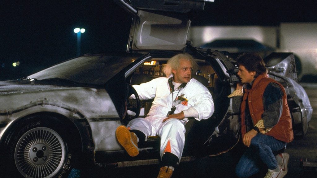 Promo image for Back to the Future showing two men talking outside a car