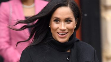Head shot of Duchess Meghan Markle in a black peacoat, stud earrings and with hair in loose waves.