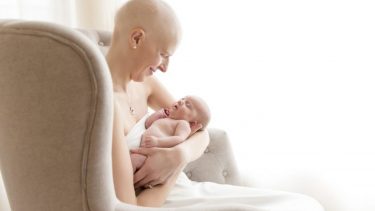 Woman with a shaved head in a white dress, poses for a picture with her newborn baby