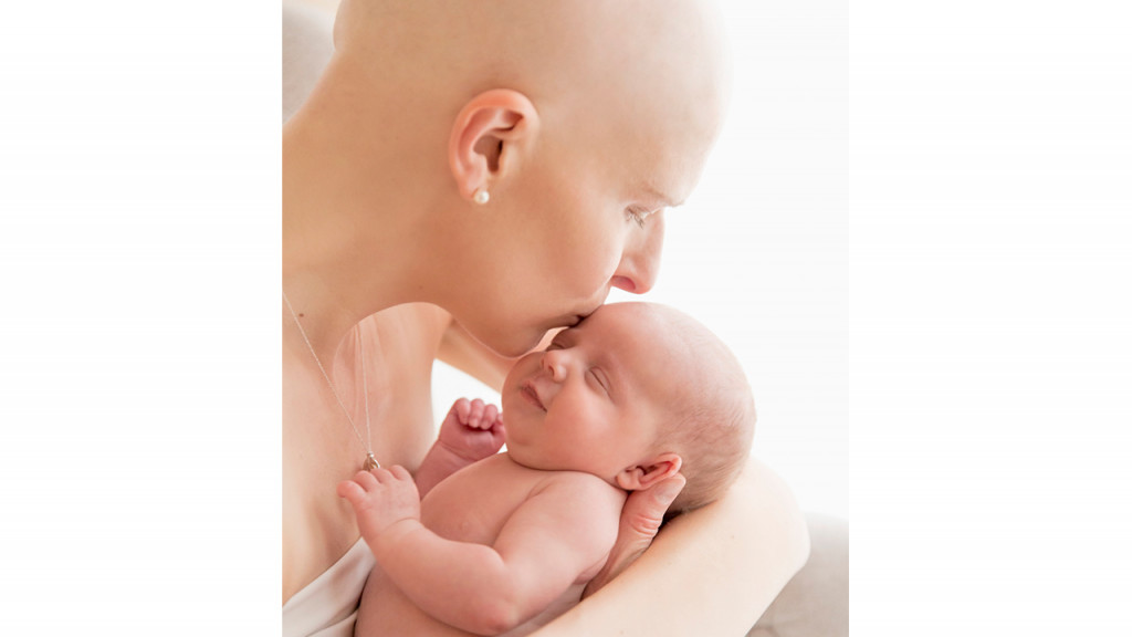 Woman with shaved head holding and kissing her baby.