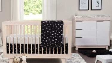A nursery decorated with a wood finished crib with a matching chest drawer. The room is decorated with a black and white themed blanket and picture frames.