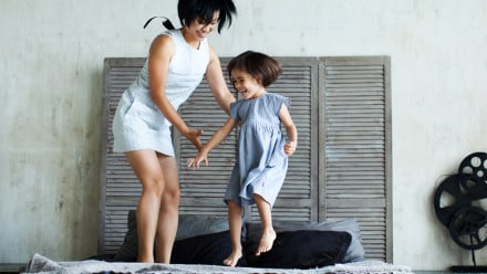 Mother and daughter jumping and laughing on a bed