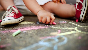 Child (only feet visible) drawing with chalk on pavement