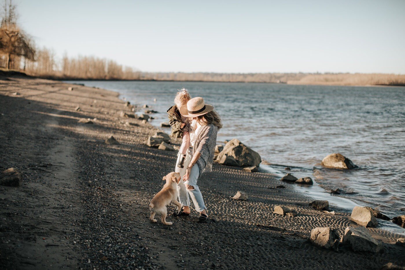 Mother and daughter hug family dog by the water