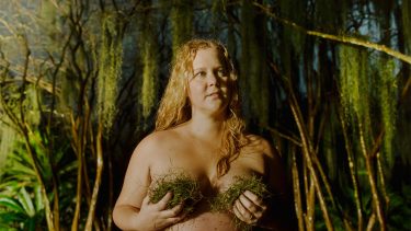 Amy Schumer holding moss to her boobs with trees in the background