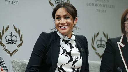 Meghan Markle smiling in a black and white printed dress and black blazer