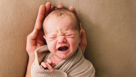 A newborn baby boy, eighteen days old, cries in his dad