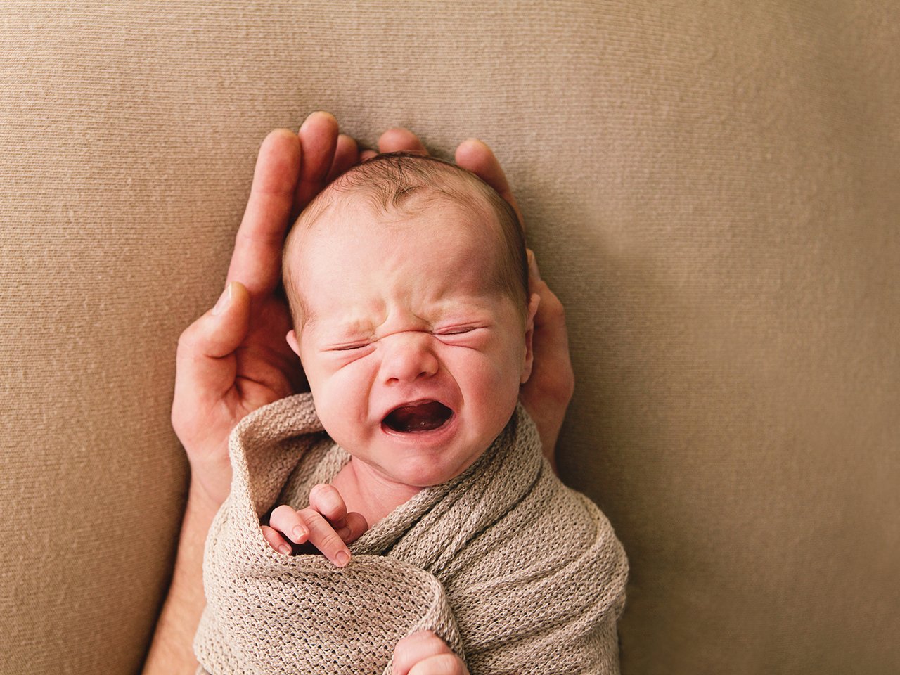 een pasgeboren jongen, achttien dagen oud, huilt in de handen van zijn vader.
