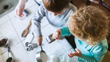 To toddler age kids learn to bake and cook together, each child helping to measure and pour out the ingredients. An enriching time of discovery for 2 and 3 year olds. Horizontal image.
