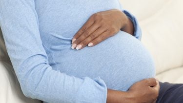 woman in blue shirt holding her pregnant belly