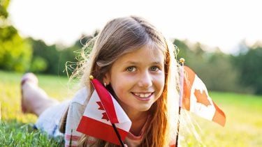 a blonde girl lying in a field holding two canadian flags