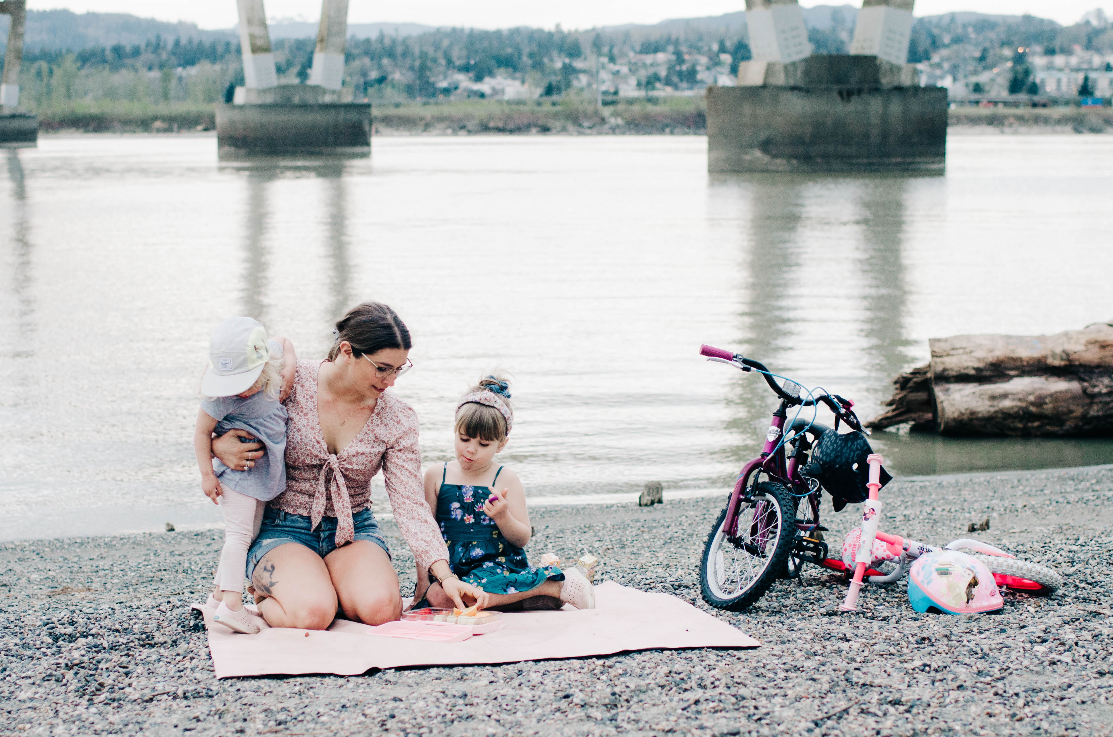Codi Lynn with her two children on a blanket by the water eating fruit, with bikes nearby