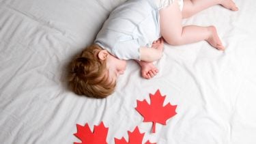 baby laying on bed with maple leaf paper cutouts