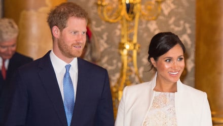 Prince Harry in a blue suit with Meghan Markle in a cream coat and metallic dress