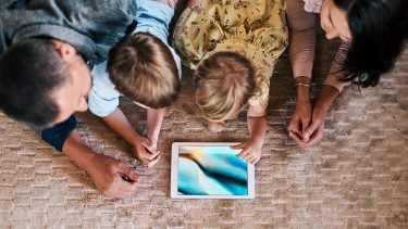 Mother, father and two sons lay on the floor around a tablet