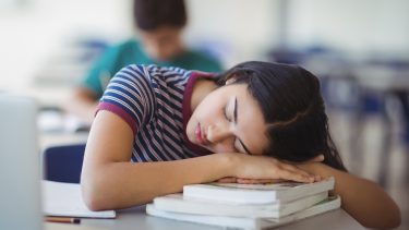 Teen sleeping on a case of books in class