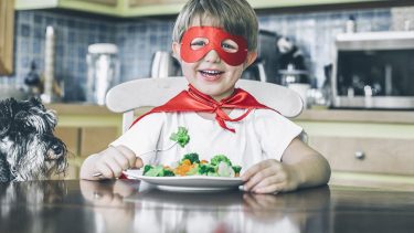 boy in red mask and cape eating vegetables