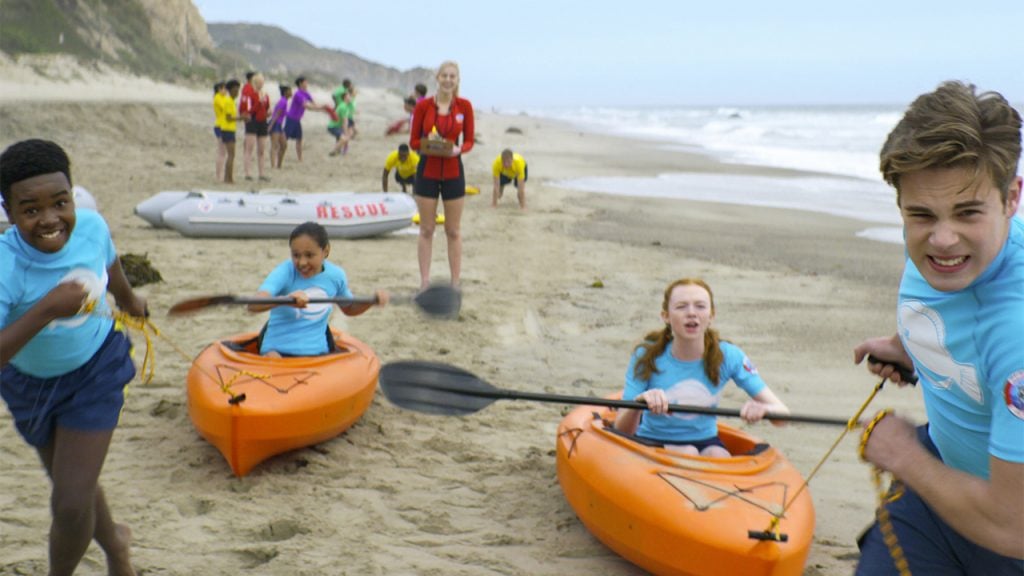 Promo image for Malibu Rescue showing two kids pulling two other kids in kayaks on the beach