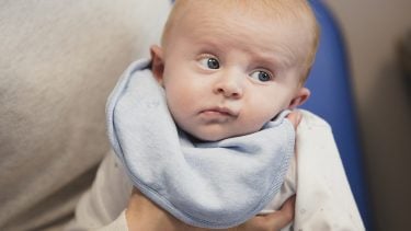 a baby being burped while wearing a blue bib and looking unimpressed