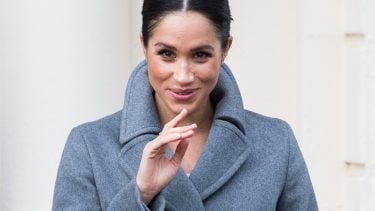 meghan markle in a grey coat with her fingers up to her face