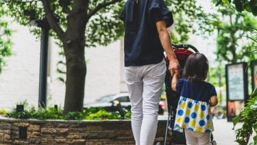 Mom pushing stroller while holding hands with young daughter outside