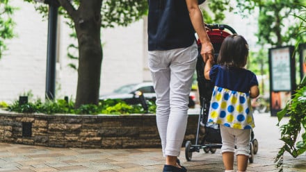 Mom pushing stroller while holding hands with young daughter outside