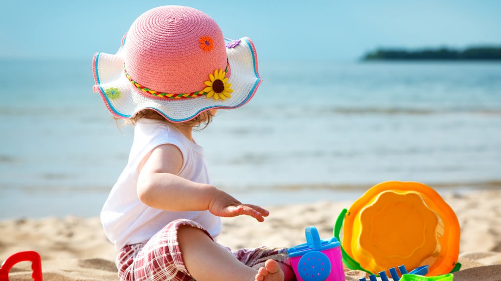 Child sitting on the beach with a sun hat
