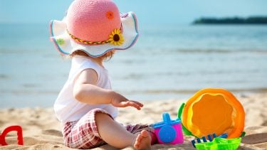 Child sitting on the beach with a sun hat