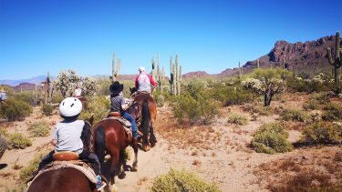 Kids riding horses through a rocky desert in Tucson
