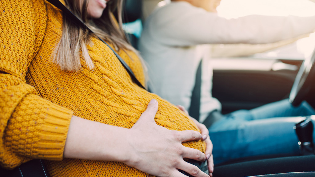 Mom holds pregnant belly in car