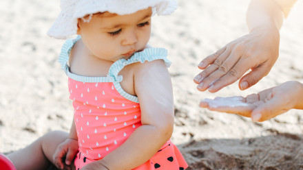 mother's hand applies sunblock to baby girl on beach