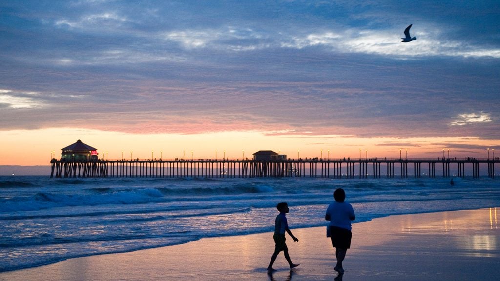 Two people walk on Huntington Beach at sunset