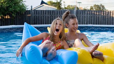 Two young girls laugh on pool floaties