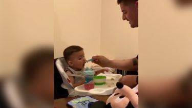 Dad feeding baby who is looking at a stuffed toy on the table