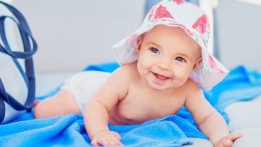 A smiling infant wearing a sun hat lays on her stomach