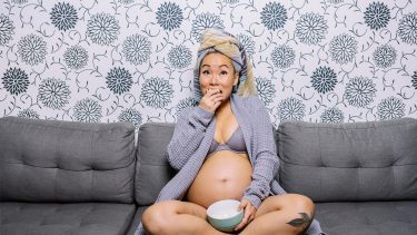 Pregnant woman eats food on the couch
