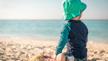 Baby sitting on beach wearing blue and green rash guard