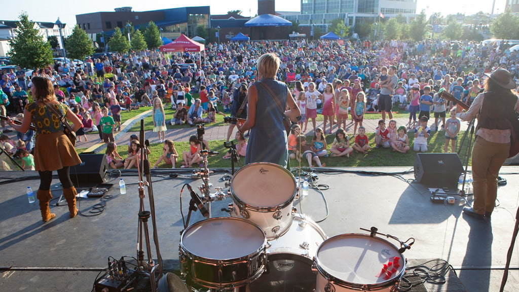 female band plays on outdoor stage with kids and families in background