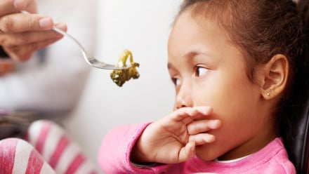 Little girl refuses to eat a piece of broccoli