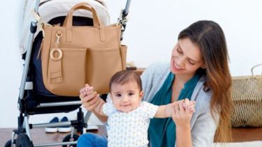 mom playing with baby with stroller and diaper bag behind them