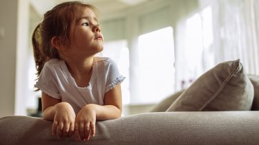 Girl looks sad as she rests on couch looking to the right